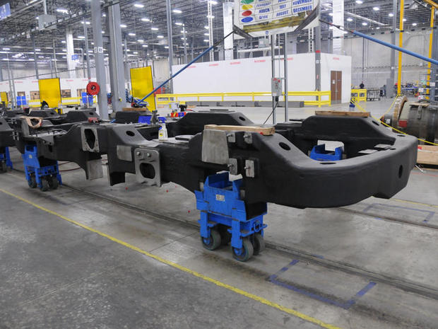 　1列のボギー台車フレームが工場の床に置かれている。これらのフレームにはやがて、車輪やそのほかのシステムが取り付けられる。