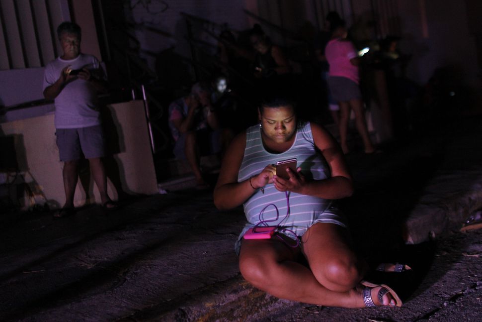 ハリケーン「マリア」の被害を受けたプエルトリコのサン・フアンで9月25日夜、携帯の電波が入る数少ない場所の1つでスマートフォンをチェックする女性