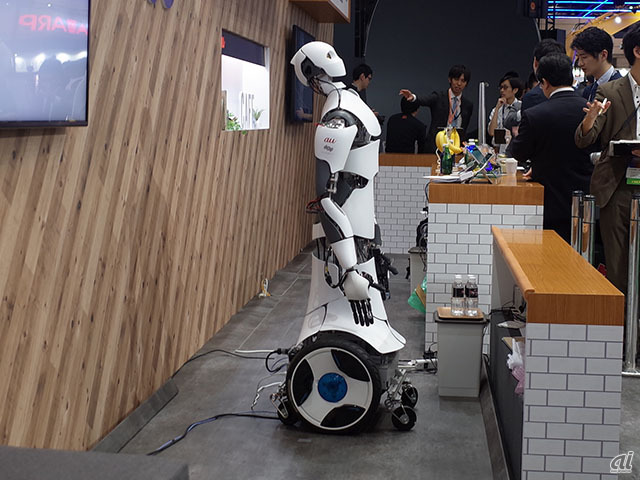 　KDDIブースでは、遠く離れた場所にあるロボットを、分身のように操作する技術を使って、カフェでロボット店員とコミュニケ―ション体験できるコーナーを用意。オペレーターと遠隔操作ロボットをクラウドでつなぎ、オペレーターはリアルタイムに動作や音声で遠隔ロボットを操作。遠隔ロボットは触覚や温度などのフィードバックを感じられ、モノを持ったり、握手したりすることもできる。
