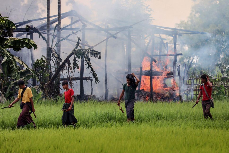 ミャンマー北部の都市マウンドー近郊の村で、炎上する家屋の前を通り過ぎる武装した男たち
