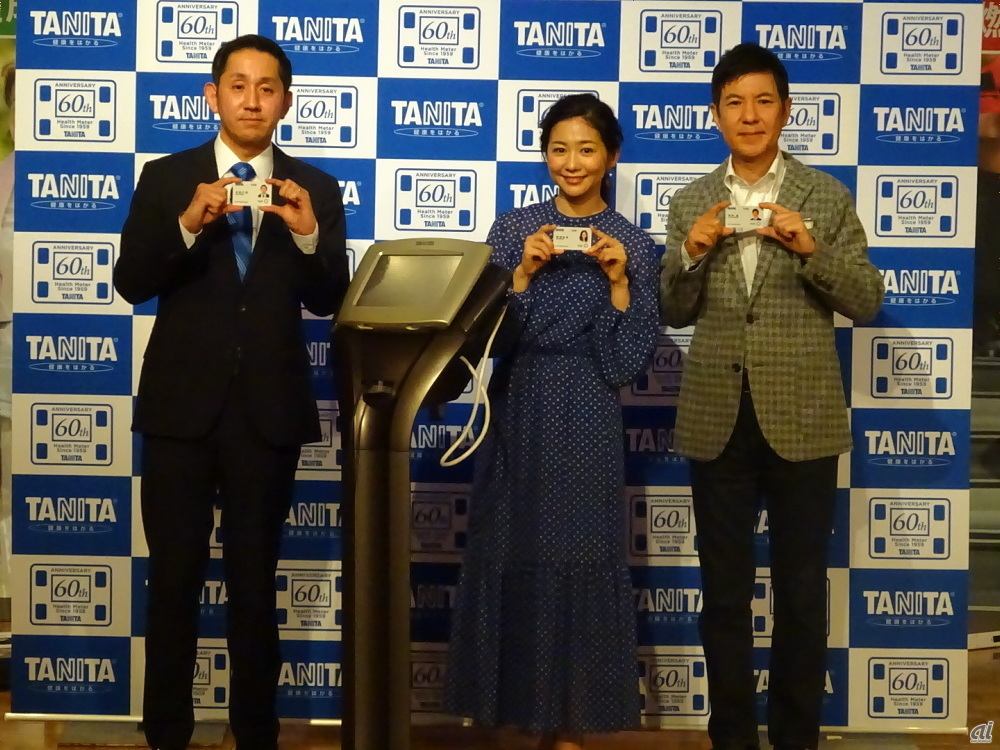タニタ 代表取締役社長の谷田千里氏、ゲストとして登場した関根勤さん、関根麻里さん。手にしているのは、カード型活動量計だ。中央の機器は脂肪燃焼モニター