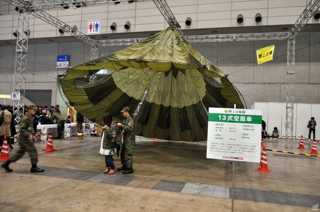 　直径約11メートルの円形状のパラシュート「13式空挺傘（ヒトサンシキクウテイサン）」。装備を背負って記念写真を撮ることもできる。