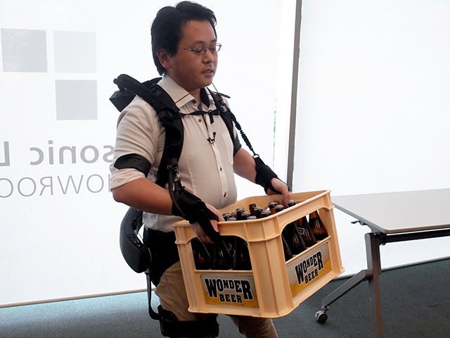 ATOUN 技術開発部次長の中野基輝氏。腕の補助機能をつけてビールケースを持ち運ぶデモを披露した