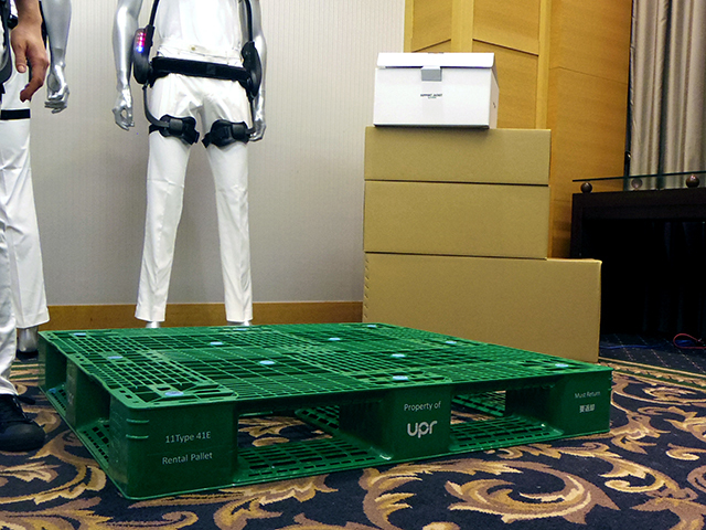 右奥に置かれたダンボールは、競合他社のアシストスーツの箱の大きさを再現したもの。一番上の白い箱が「サポートジャケットEp+ROBO」の箱で、大幅に小型化されていることがわかる