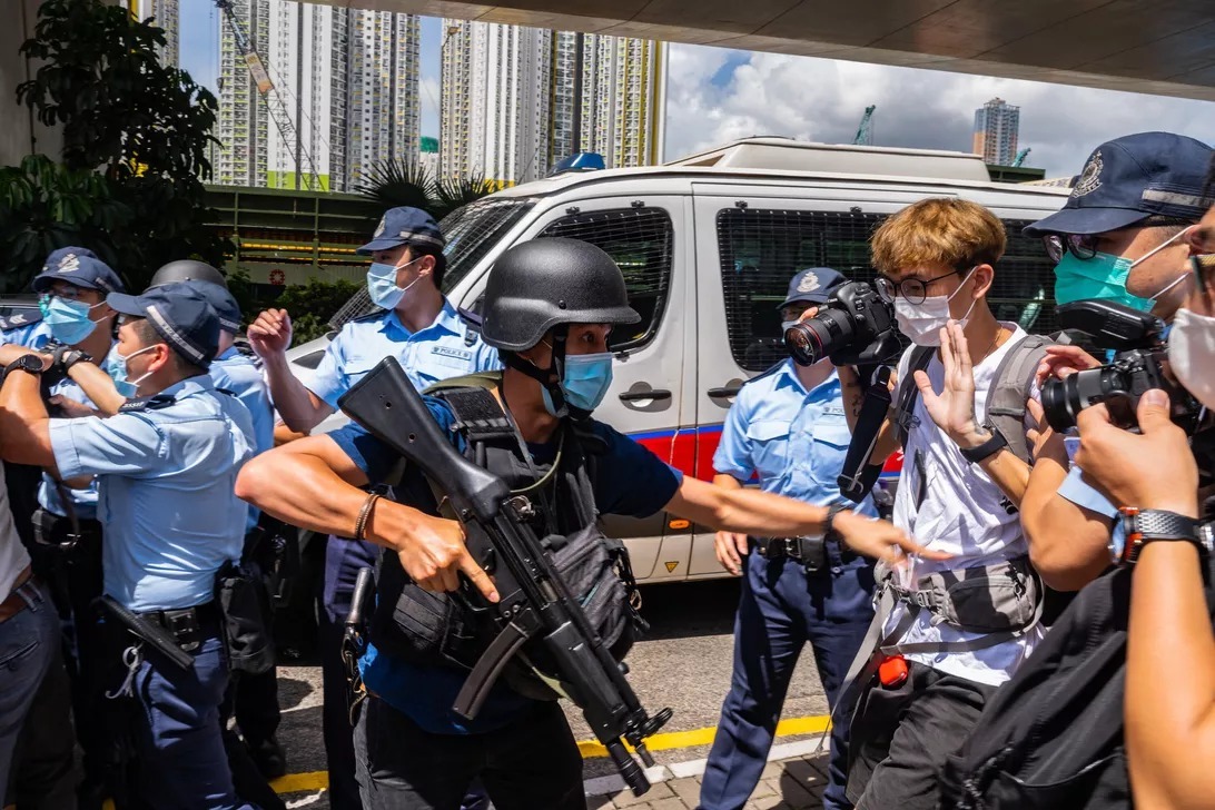 香港国家安全維持法に違反したとして初めて起訴された男性が裁判所に向かうのをガードする警官ら