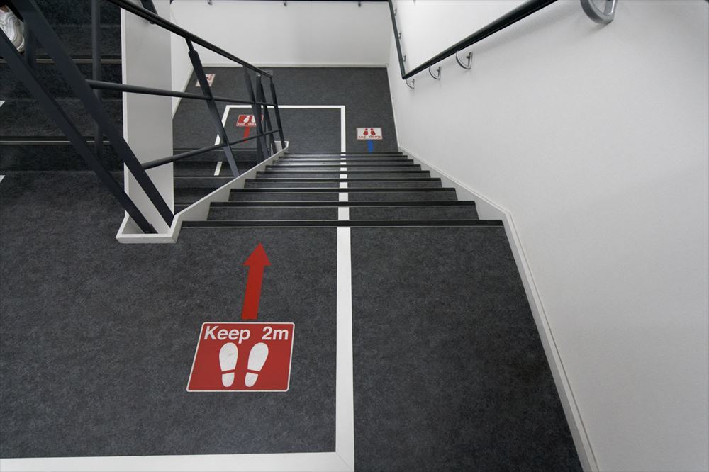 廊下や階段の床には、他の人と2メートルの距離を保つようマークやラインで指示がある