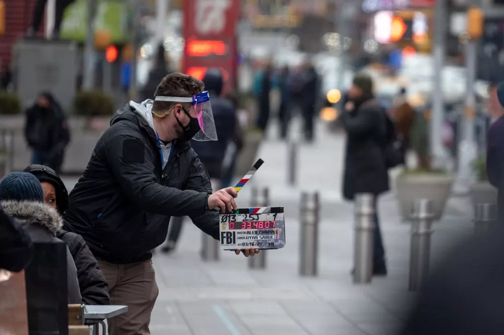 A person wearing a mask and face shield uses a clapboard during the filming of a TV series in Times Square this past March.