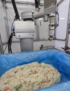 ポテトサラダのような不定形かつ粘着性の高い惣菜を、高い重量精度で連続的に容器に盛り付けられるロボット技術の実用化に向けた取り組み