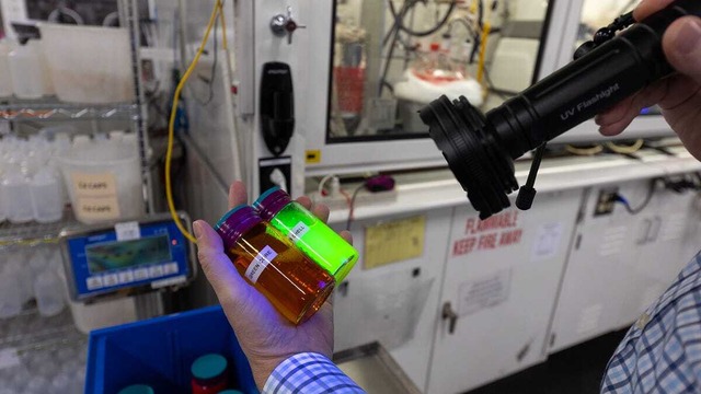 　Nanosysの最高経営責任者（CEO）兼プレジデントであるJason Hartlove氏が、2本の瓶に紫外線を当てているところ。中には、製造工程の段階が異なる量子ドットが入っている。
