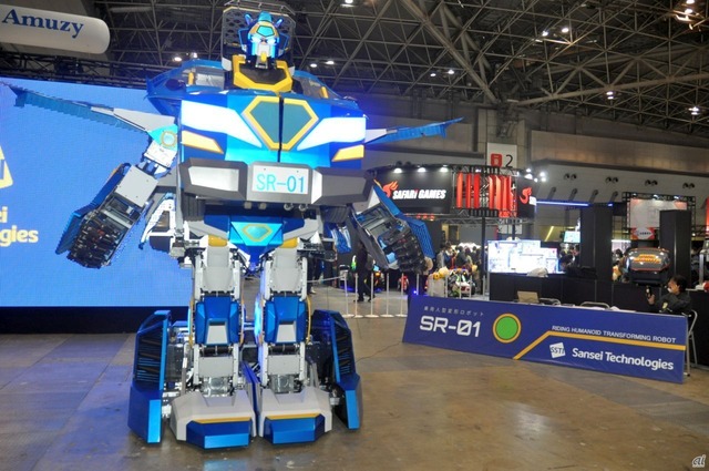 　人型変形ロボットのSR-01。二足歩行で移動可能な人型（ロボットモード）と、車輪走行で移動可能な車型（ビークルモード）に変形できる、全高約4メートルのロボット。最大2人まで搭乗可能で、運転席での操作のほか、無線での遠隔操作も可能としている。